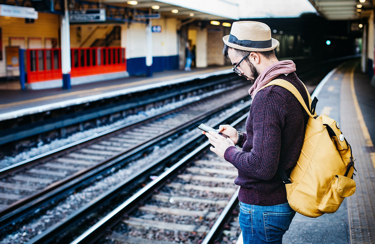 Homme au bord d'un quai de gare, téléphone à la main