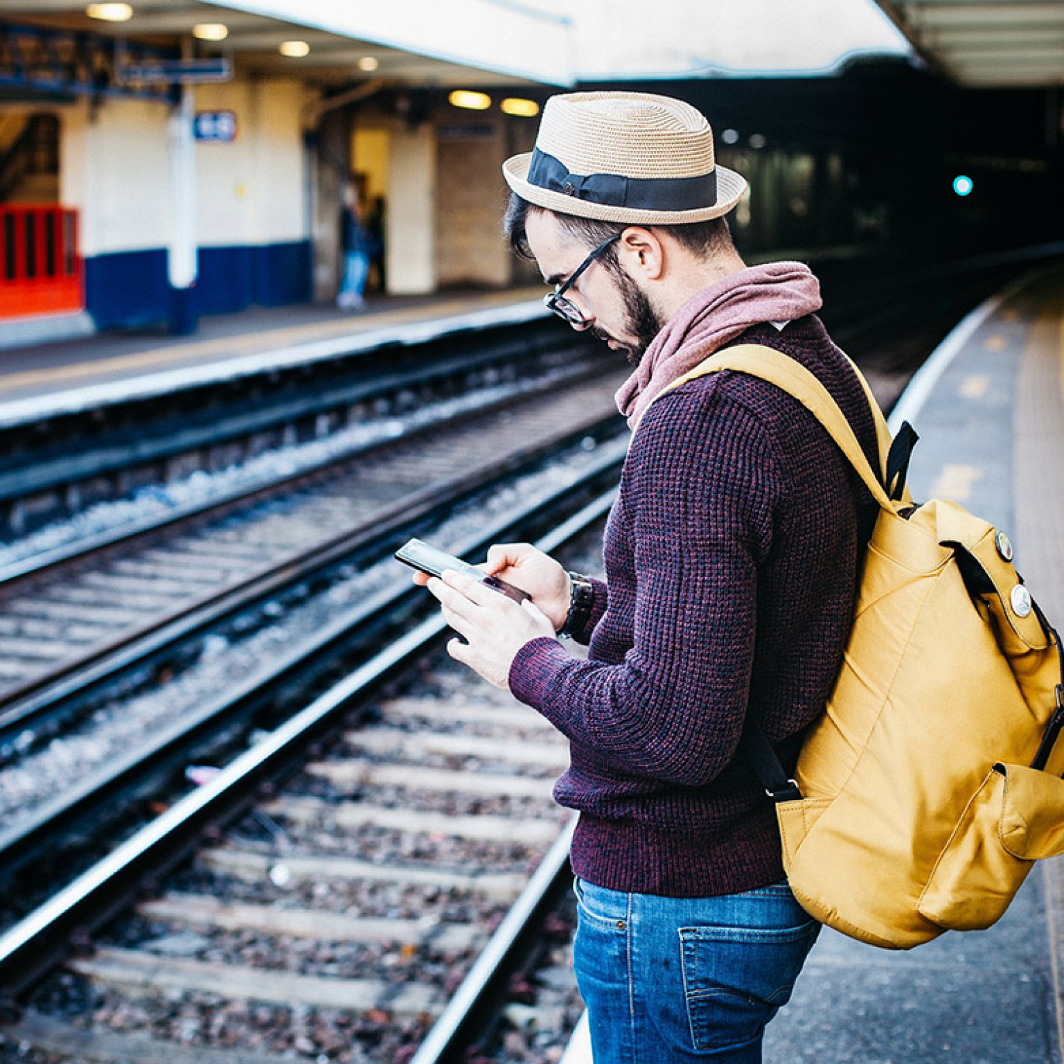 Homme au bord d'un quai de gare, téléphone à la main